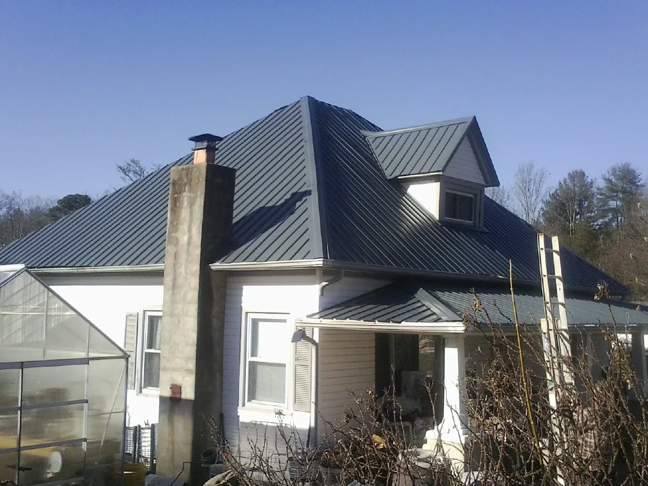 Dark blue standing seam metal roof on a white farmhouse with dormer — Slate & Tile Roof Repair by Roofing Brothers in Hill Afb