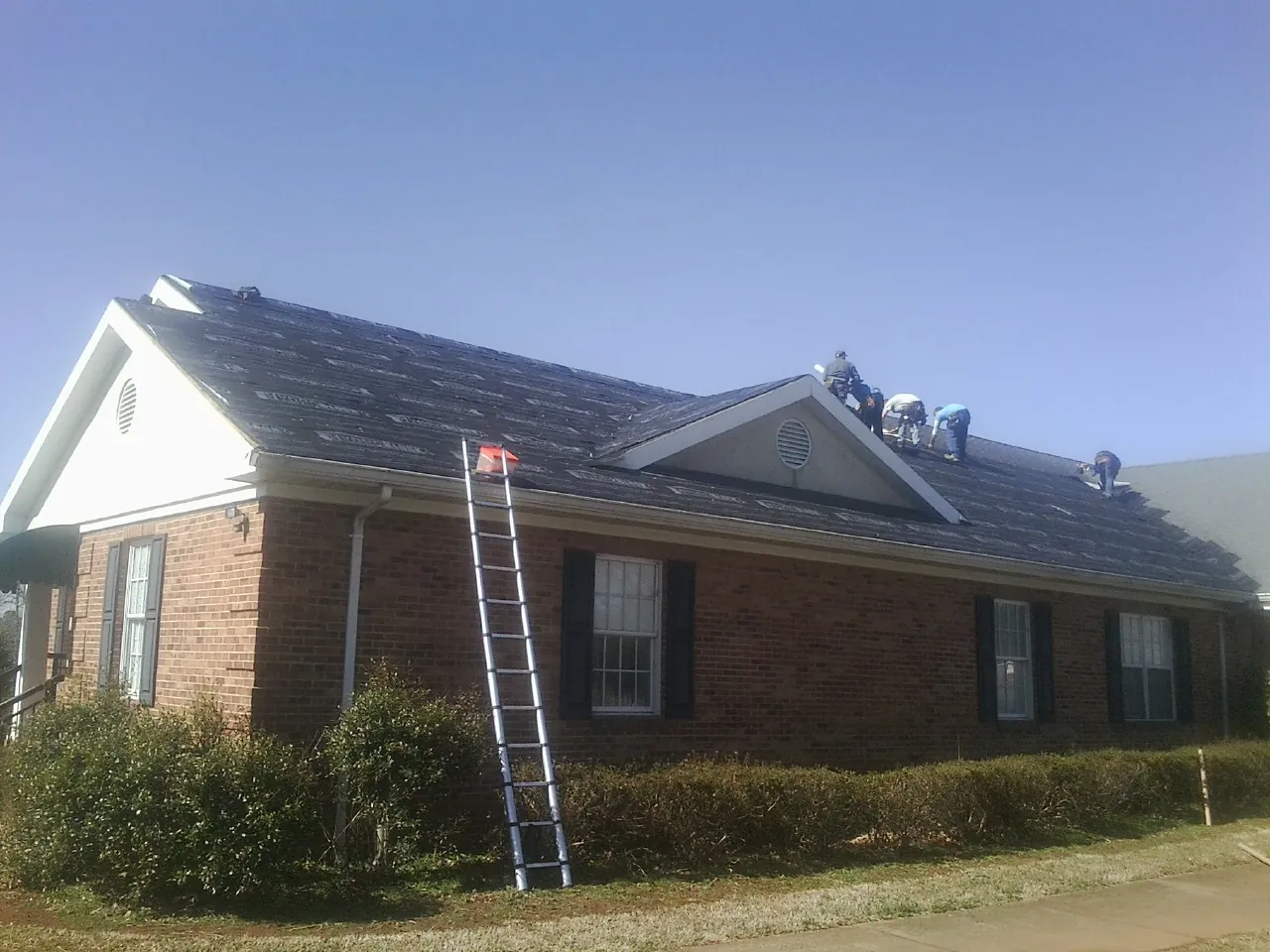 Crew tearing shingles off a brick ranch roof with a ladder set — Emergency Roof Repair work by our crew in Hill Afb