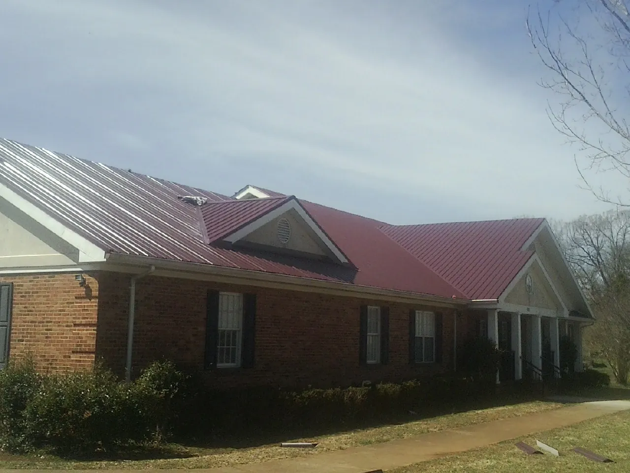 Red metal roof with gabled entries on a long brick building, from a Hail Damage Roof Repair job in Hill Afb