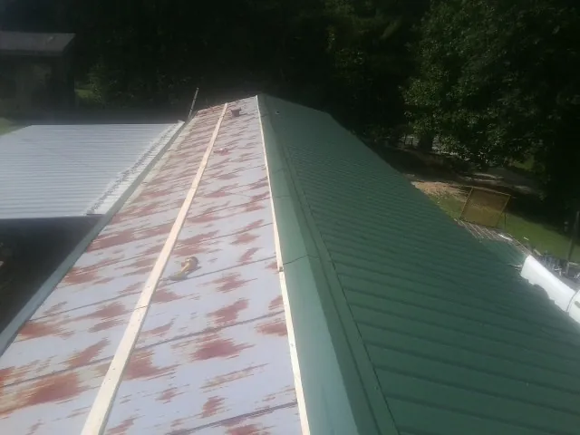 Old rusted panels beside newly installed green metal roofing — Wind Damage Roof Repair by Roofing Brothers in Hill Afb