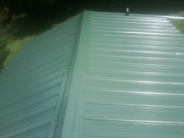New green metal panels meeting at the ridge of a roof — Flat Roof Repair work by our crew in Hill Afb