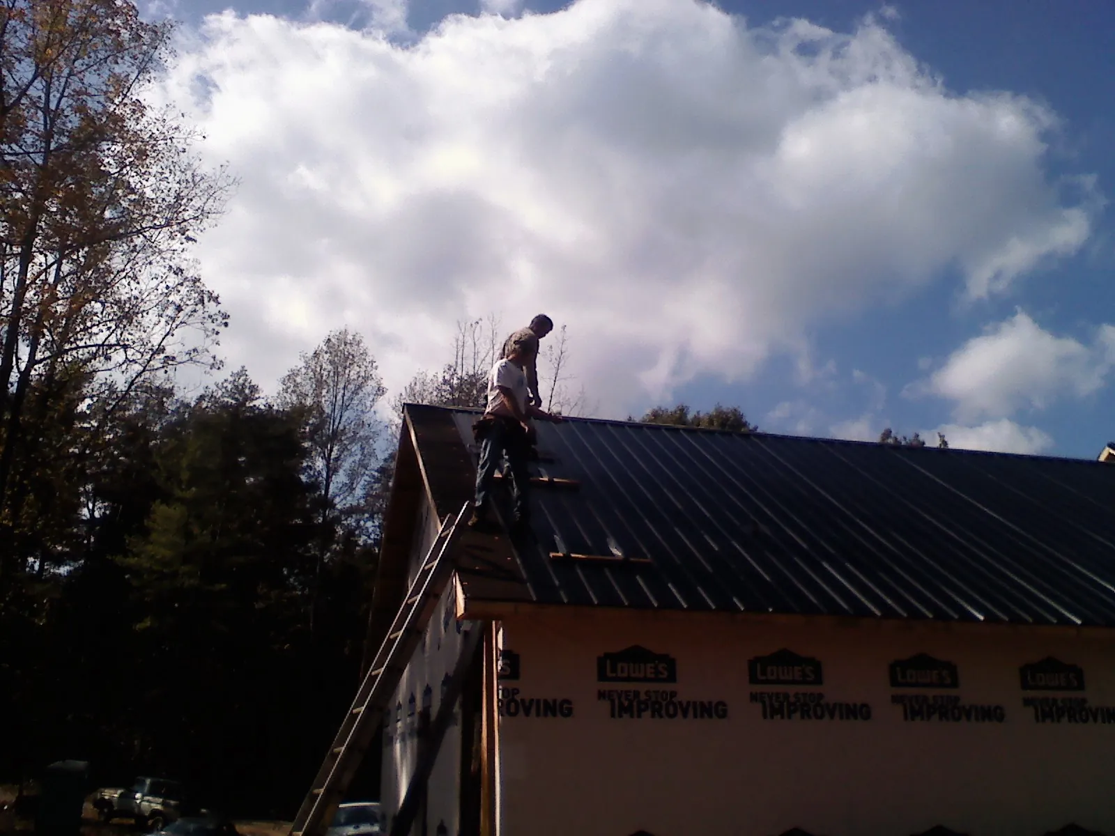 Roofer fastening dark metal panels high against a cloudy sky, from a Roof Inspection job in Hill Afb