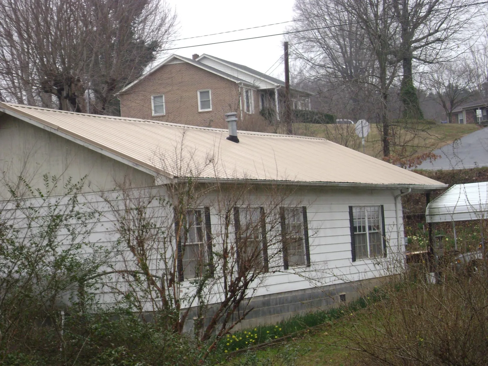 Tan metal roof on a white sided house set into a hillside — Commercial Roofing by Roofing Brothers in Hill Afb