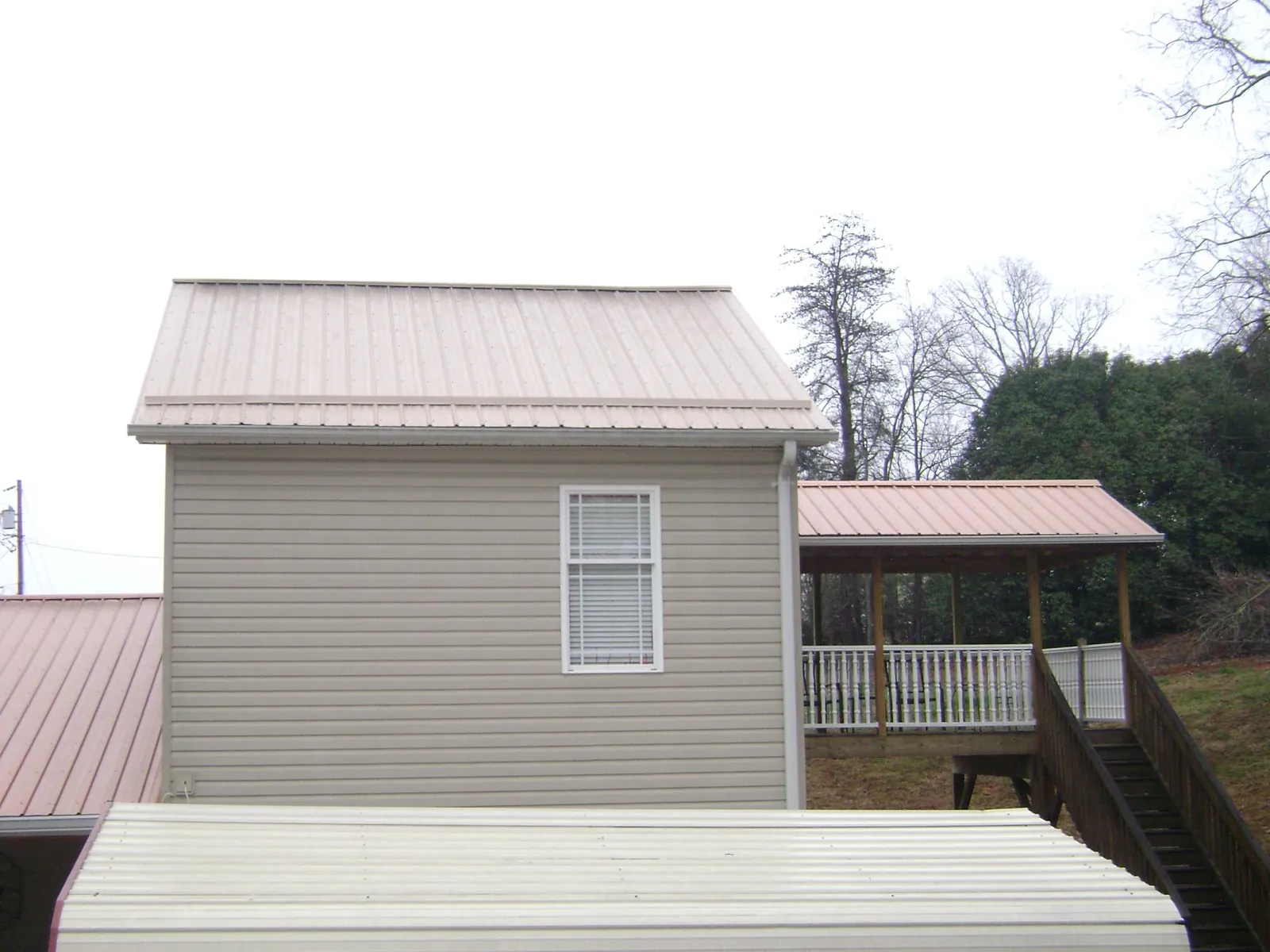 Tan metal roofs on a two story addition and attached porch, from a Roof Replacement job in Hill Afb